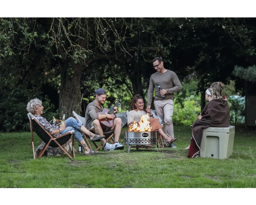 Eine Gruppe von Menschen sitzt um eine Feuerschale im Freien und genießt die Zeit zusammen.