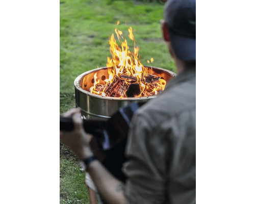 Mann mit Gitarre sitzt vor einer Feuerstelle im Garten