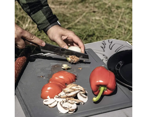 Gemüse wie Paprika, Tomaten, Zwiebeln und Champignons werden auf einem Schneidebrett geschnitten.