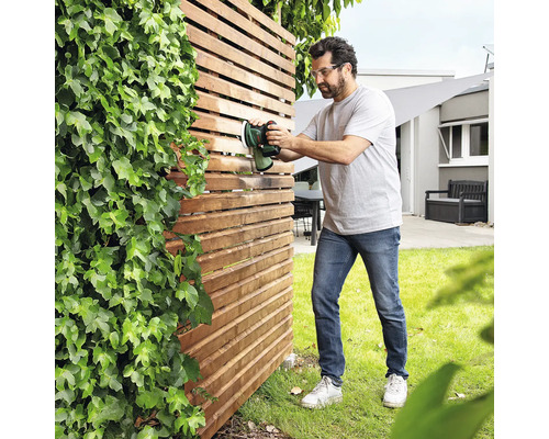 Mann behandelt Holzzaun mit Farbsprühgerät im Garten.
