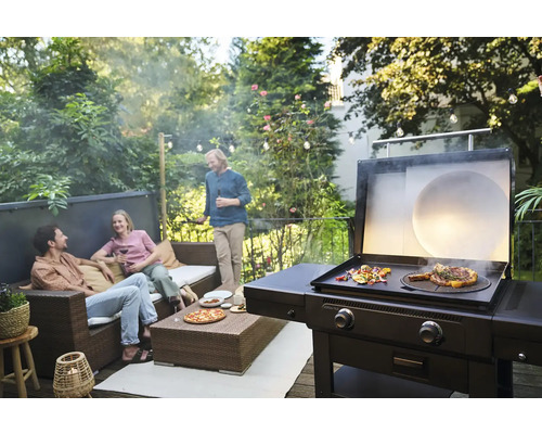 Szene mit Grill, auf dem Essen zubereitet wird, und Personen, die sich auf einer Terrasse unterhalten.