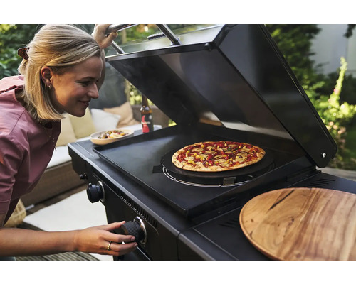Frau bereitet Pizza auf einem schwarzen Gasgrill zu.