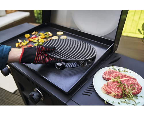 Eine Person bereitet Gemüse und Fleisch auf einem Grill zu.