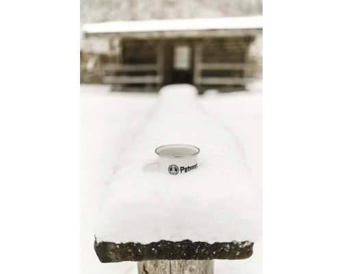 Emailletasse mit Petronam Logo im Schnee vor Holzhütte