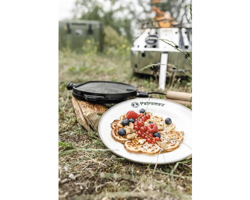 Szene im Freien mit Pfannkuchen auf einem Teller, einer gusseisernen Pfanne und einem Kocher