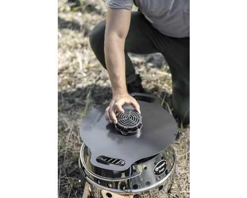 Person hockt und befestigt einen Aufsatz auf einem Petromax Atago Grill.