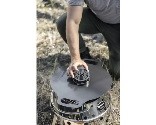 Eine Person platziert einen Deckel mit einem runden Aufsatz auf einem Petromax Atago Grill.