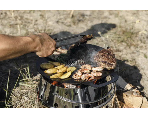 Person grillt Steaks, Kartoffeln und Garnelen auf einer Feuerplatte