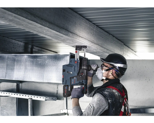 Mann bohrt mit einem Bohrhammer in eine Betondecke, inklusive Staubabsaugung.