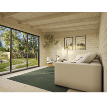 Innenraum eines Holzhauses mit Sofa, Tisch und Ausblick in den Garten
