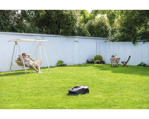 Szene mit einem Rasenmähroboter auf einer Rasenfläche, während eine Person in einer Gartenschaukel entspannt.