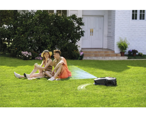 Szene mit Rasenmähroboter im Einsatz während sich ein Paar auf dem Rasen entspannt