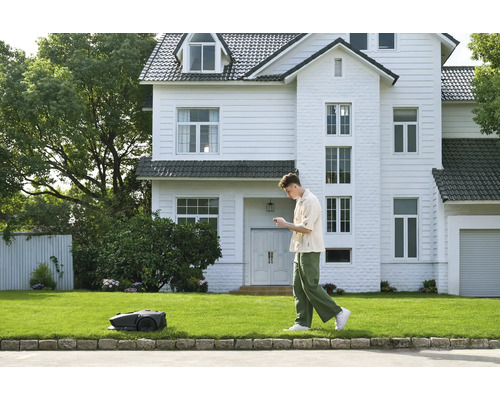Ein Mann bedient einen Rasenmähroboter vor einem Haus.