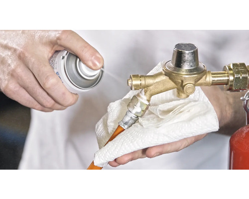 Eine Person reinigt mit einem Spray und einem Tuch einen Gasdruckregler.