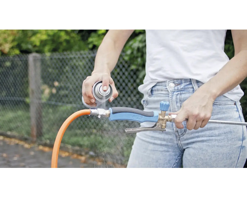 Eine Person sprüht ein Reinigungsmittel auf einen Wasserstrahlregler, der an einem Gartenschlauch befestigt ist.