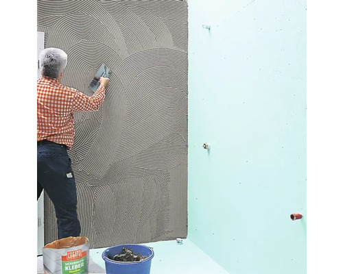 Ein Handwerker trägt Fliesenkleber auf eine Wand im Badezimmer auf.