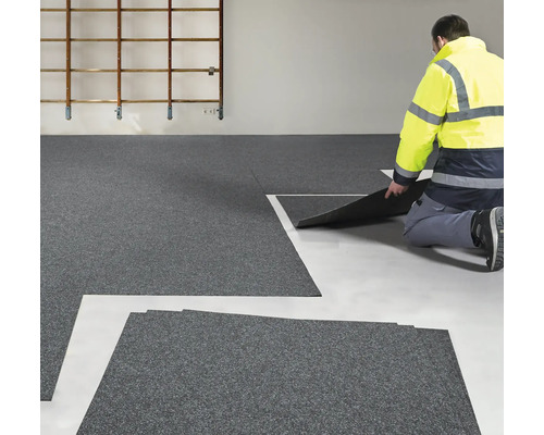 Verlegung von grauen Bodenfliesen in einem Raum durch einen Handwerker.