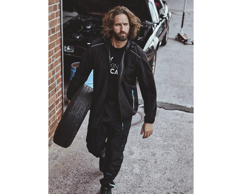 Mann in Arbeitskleidung trägt einen Reifen vor einer Autowerkstatt