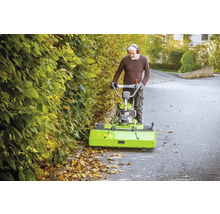 Mann benutzt eine Kehrmaschine zur Laubentfernung auf einer Straße.