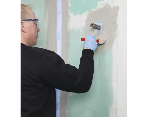 Handwerker spachtelt Wand mit Spachtelmasse und Werkzeug