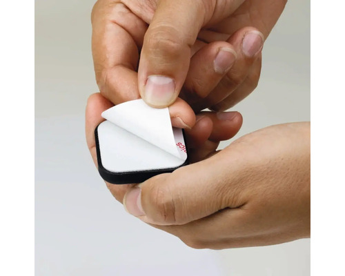 Eine Hand zieht die Schutzfolie von einem selbstklebenden Möbelgleiter ab.