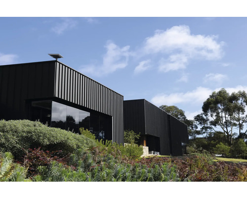 Modernes Gebäude mit vertikalen Fassadenelementen und großen Glasfenstern umgeben von Grünanlage unter blauem Himmel