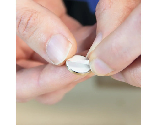 Eine Person entfernt die Schutzfolie von einem Scheibenmagneten.