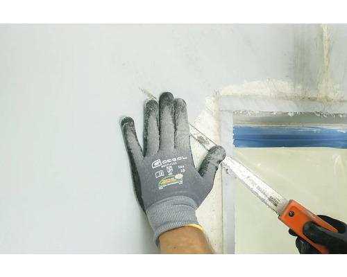 Eine Hand in einem Arbeitshandschuh sägt mit einer Handsäge an einer Wand.