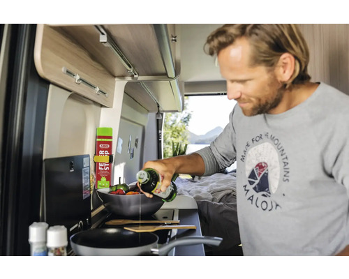 Mann kocht in einem Wohnmobil und gießt Öl in eine Pfanne.