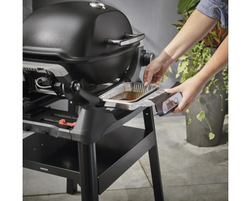 Frau setzt eine Tropfschale in einen Weber Grill ein.
