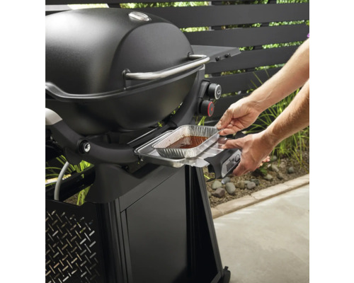 Weber Grill mit Person, die eine Tropfschale einsetzt