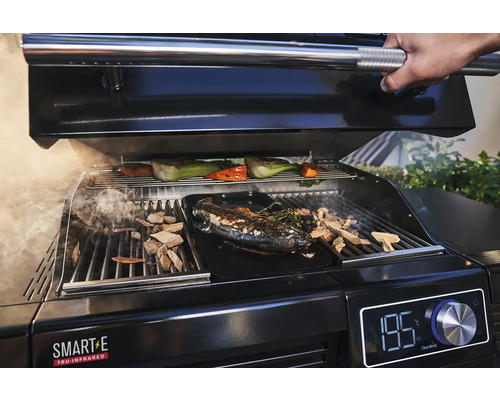 Ein Grill mit Fisch, Gemüse und Holzspänen wird zubereitet.