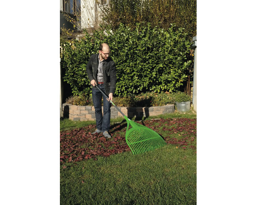 Mann harkt Blätter mit einem Laubbesen im Garten.