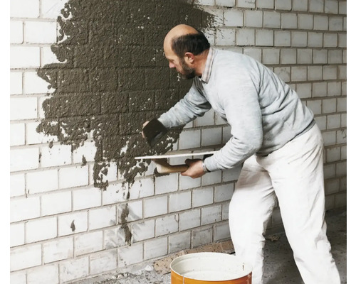 Mann trägt Putz auf eine Ziegelwand auf