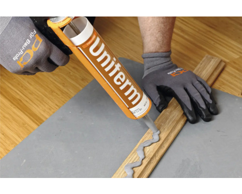 Eine Person trägt Handschuhe und verwendet eine Kartuschenpistole zum Auftragen von Klebstoff auf ein Holzstück.