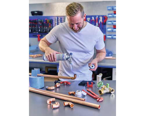 Mann lötet Kupferrohre mit einem Gasbrenner und Werkzeugen auf einem Tisch.