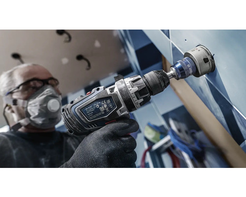 Handwerker bohrt mit einer Bohrmaschine ein Loch in eine geflieste Wand