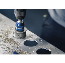 Eine Lochsäge bohrt ein Loch in ein Metallblech mit herumliegenden Metallspänen.