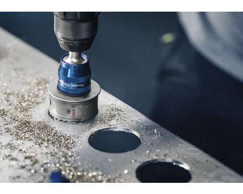 Eine Lochsäge bohrt ein Loch in ein Metallblech mit herumliegenden Metallspänen.