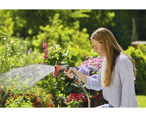 Frau gießt Pflanzen mit einem Gartenschlauch in einem Garten