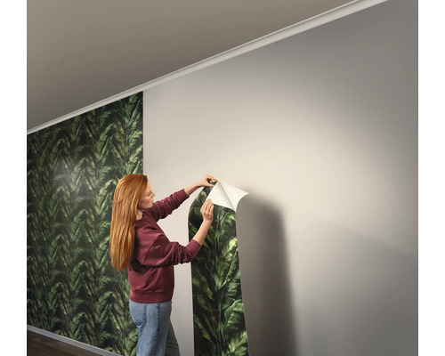 Frau bringt Tapete mit Blattmuster an der Wand an
