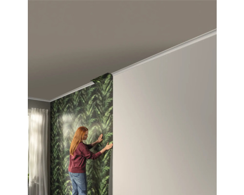 Frau bringt Tapete mit Blattmuster an der Wand an