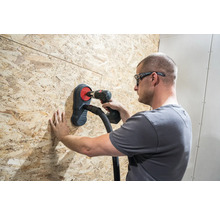 Handwerker bohrt mit einer Bohrmaschine durch eine Holzplatte mit Staubabsaugung