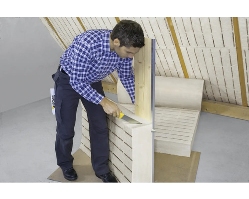 Mann schneidet Dämmwolle mit einem Messer in einem Dachgeschoss zu.