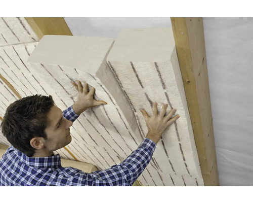 Mann befestigt flexible Holzfaser-Dämmplatten zwischen den Sparren