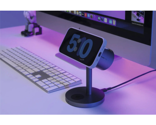 Smartphone auf Ladestation neben Computertastatur und Monitor.