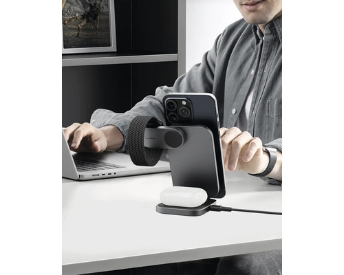 Person arbeitet am Laptop mit kabelloser Ladestation für Mobiltelefon und Ohrhörer auf dem Schreibtisch