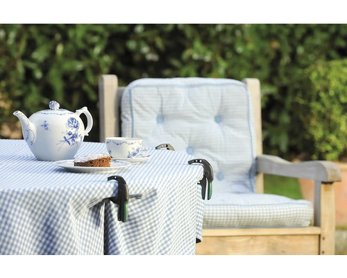 Gedeckter Gartentisch mit Teekanne, Tasse, Kuchen und Tischdeckenklammern auf karierter Tischdecke neben einem Stuhl mit Kissen