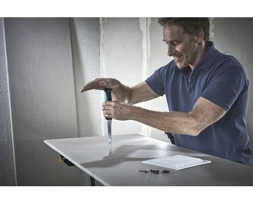 Ein Mann sägt eine Gipskartonplatte mit einer Säge auf einer Werkbank.