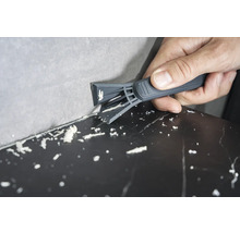 Eine Person entfernt mit einem Fugenkratzer Silikonfugen zwischen Wand und Oberfläche.